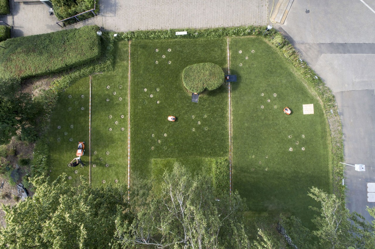 Overhead view of a green space on the factory grounds divided into four, with STIHL robotic mowers and a manual lawn mower