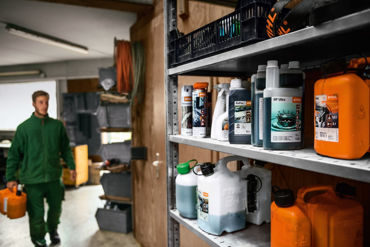 Various STIHL fuels and lubricants on a shelf, with a man in the background holding a canister for transporting hazardous goods