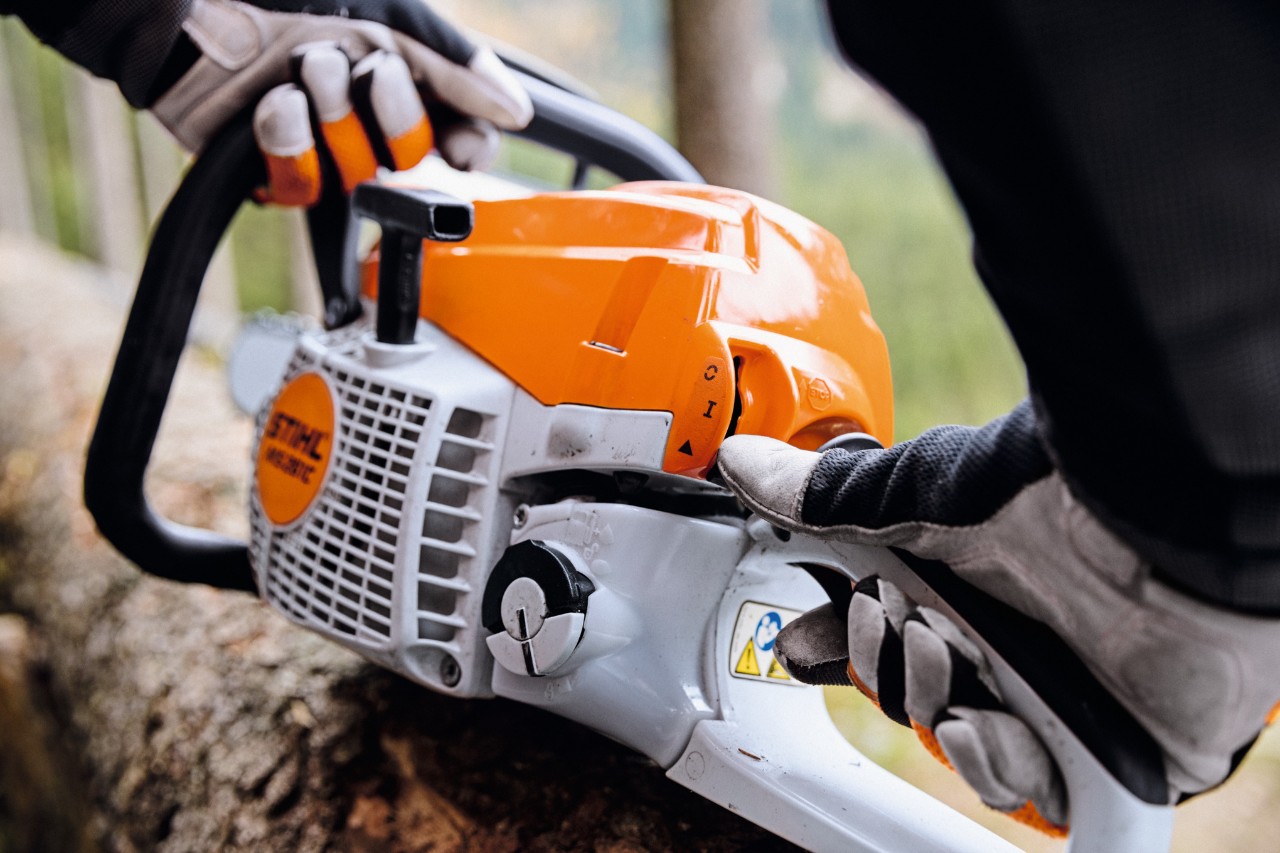 Close-up of a STIHL MS 261 C-M petrol chainsaw being started by a person wearing protective gloves