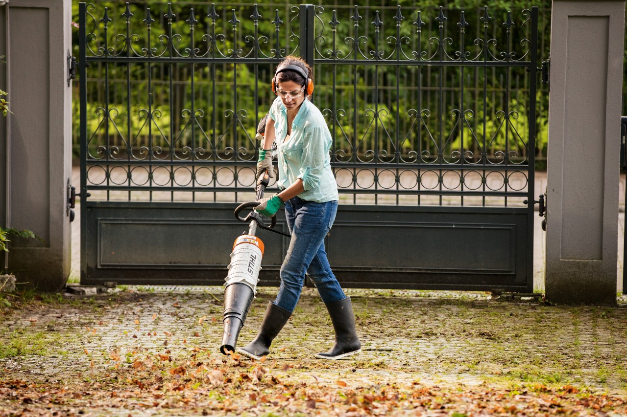 A woman wearing safety protection using a STIHL KM 131 R KombiEngine with blower attachment to collect leaves