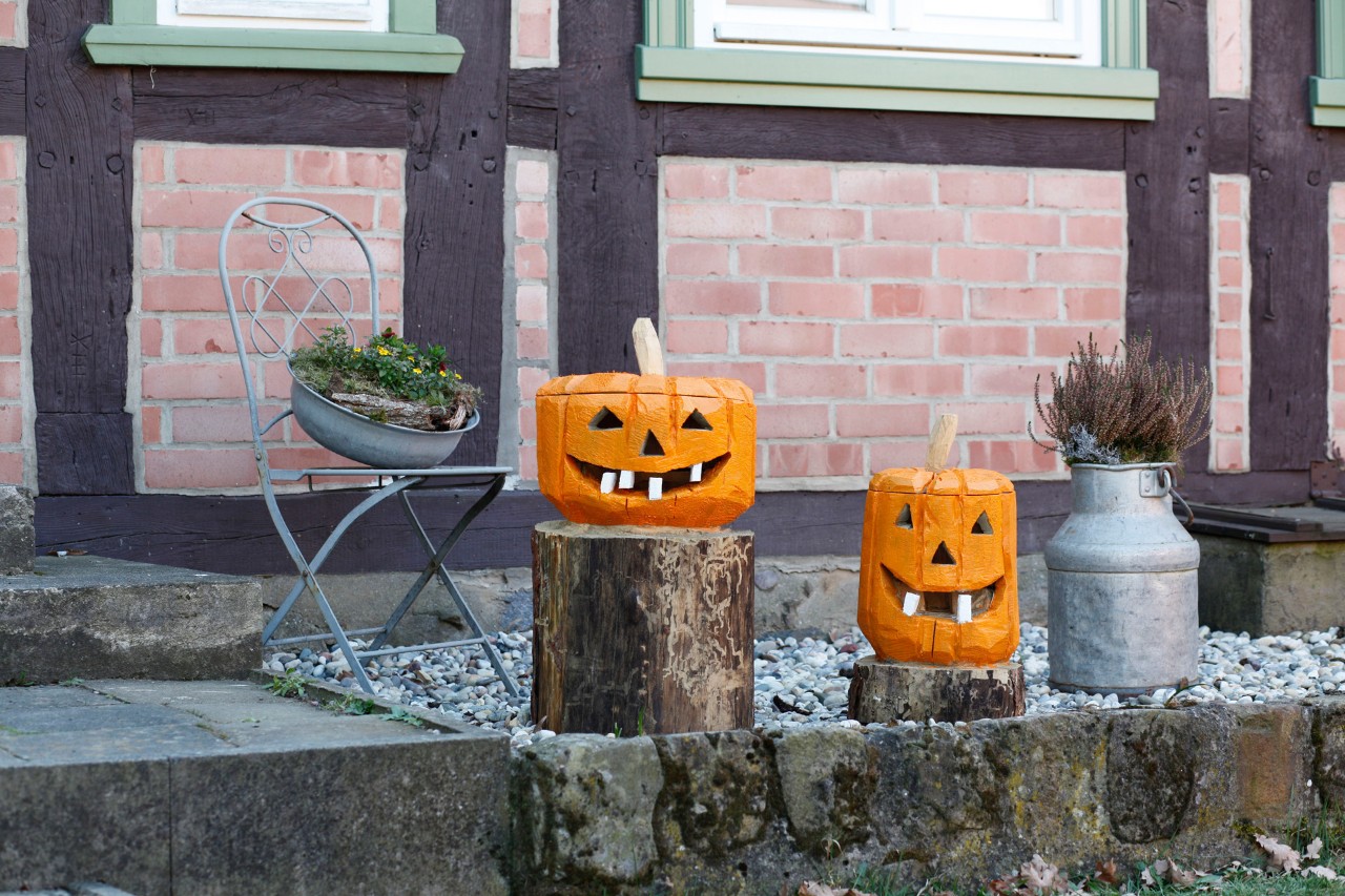 Two tree stumps each with a wooden pumpkin on them, as decoration in front of a house