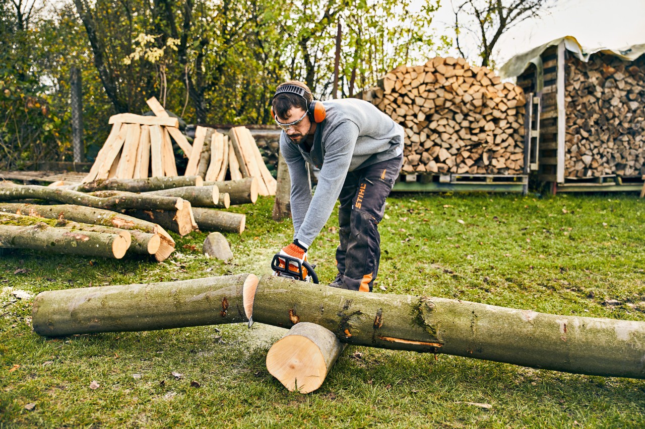 A man cutting a tree trunk with a STIHL MS 180 petrol-driven chainsaw in order to build a plant trough.