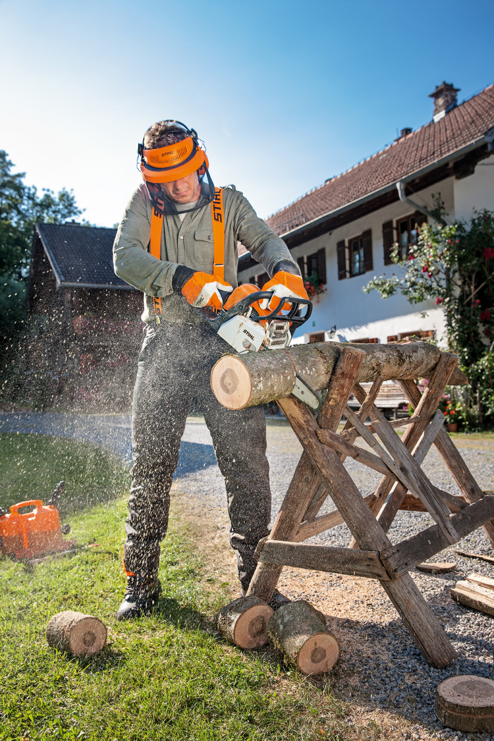 A man wearing protective clothing uses a STIHL MS 170 petrol-driven chainsaw to cut through a tree trunk on a sawhorse.