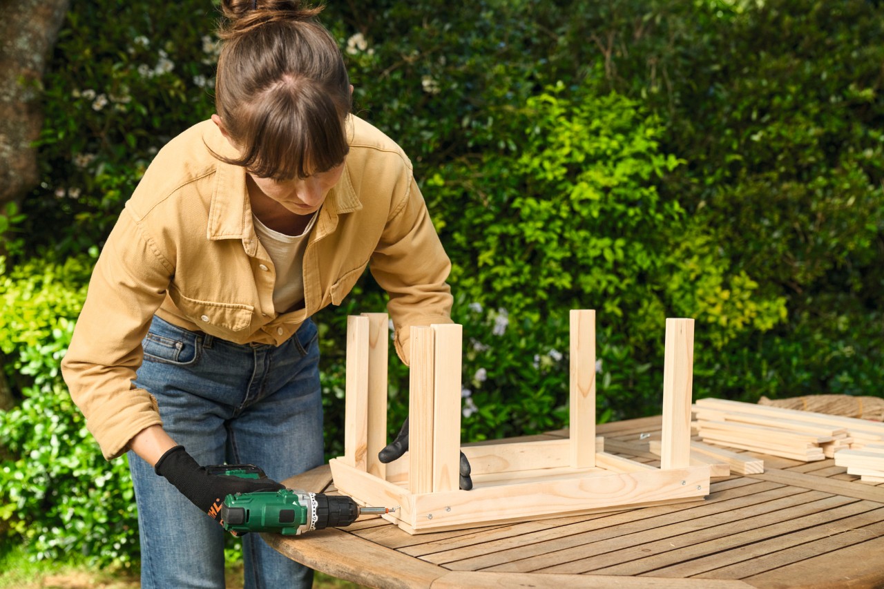 A woman screws together the wooden strips for the planter on the short sides