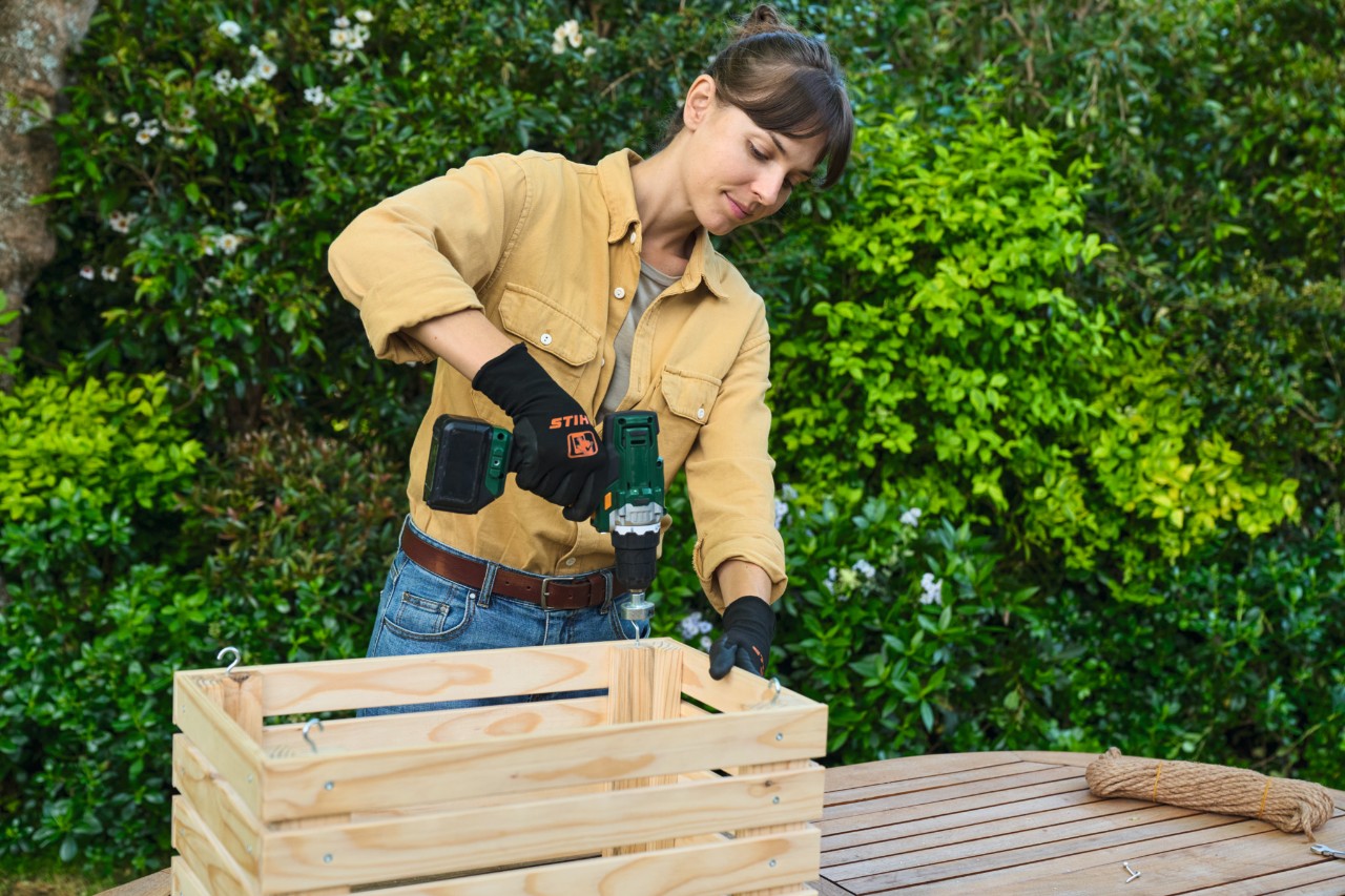 A woman attaches hooks to a DIY planter to enable it to be hung up later 