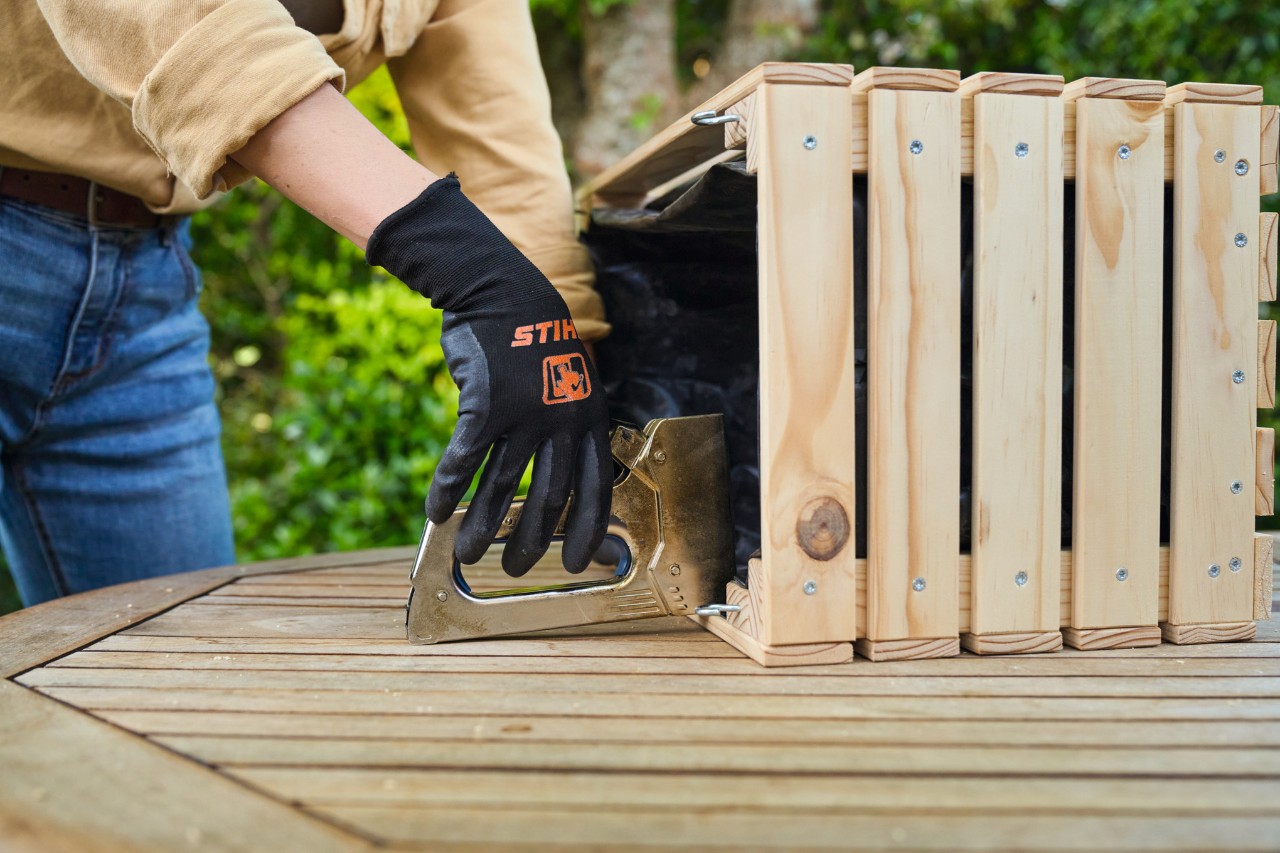 A woman lines the DIY planter with waterproof sheet and staples it in place