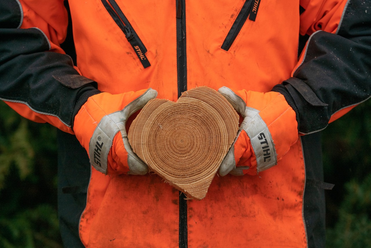 A person wearing protective clothing holds a heart carved from wood