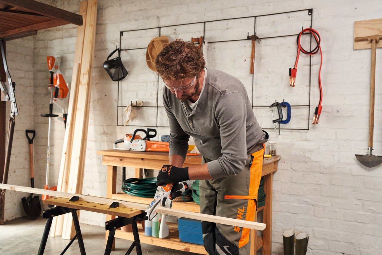 A man sawing thin wooden boards in a workshop with the STIHL GTA 26 cordless garden pruner, with a tool wall in the background