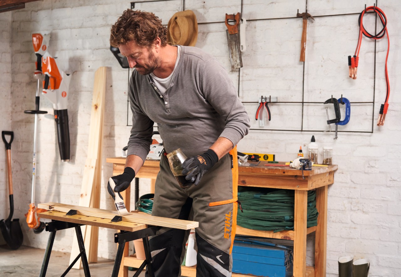 A man at a workbench oiling wooden components for a potting bench