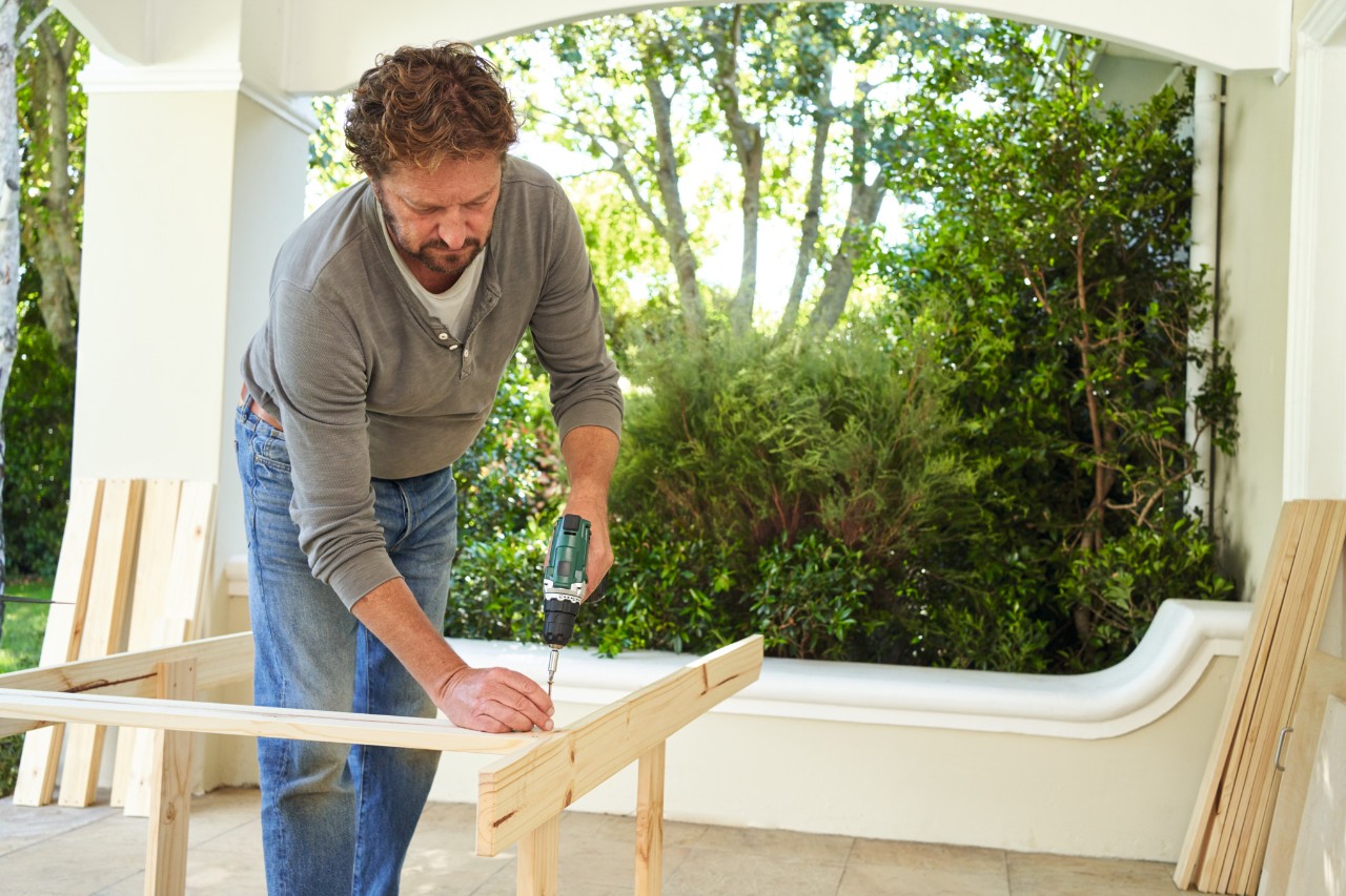 A man on a terrace screwing together the frame for a potting bench