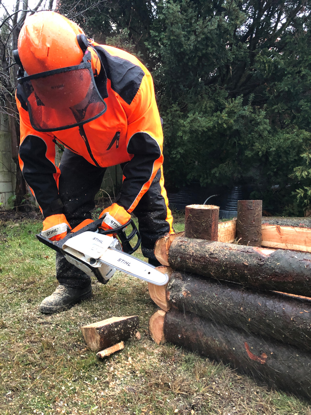 A man wearing protective gear uses a STIHL MS 170 chainsaw to trim overhanging wood from the corner of a raised bed