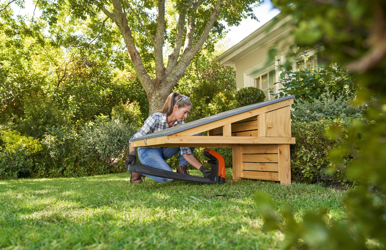 Woman wearing safety glasses and work gloves places the STIHL iMOW® robotic mower docking station under the DIY garage 