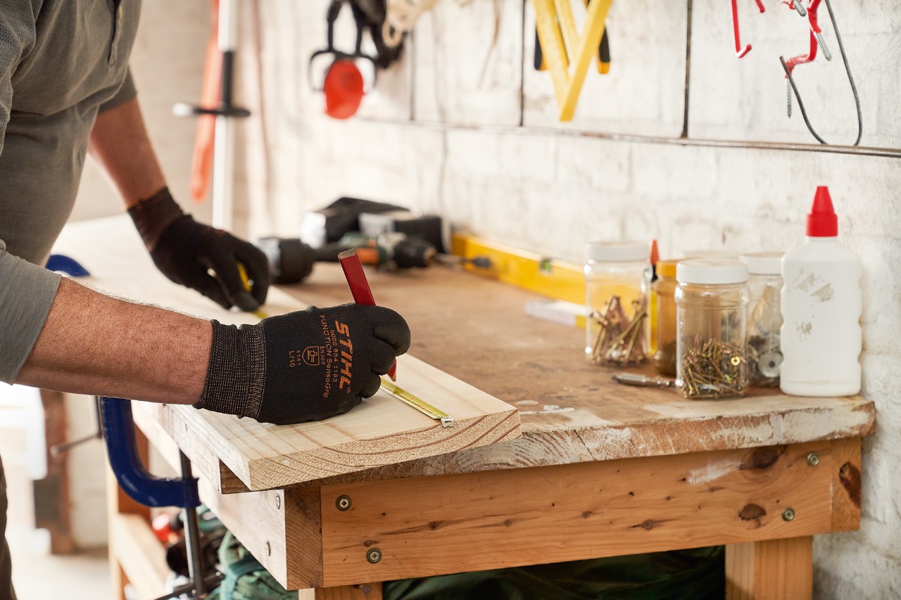 A man wearing STIHL protective gloves marking drill holes on a wooden board