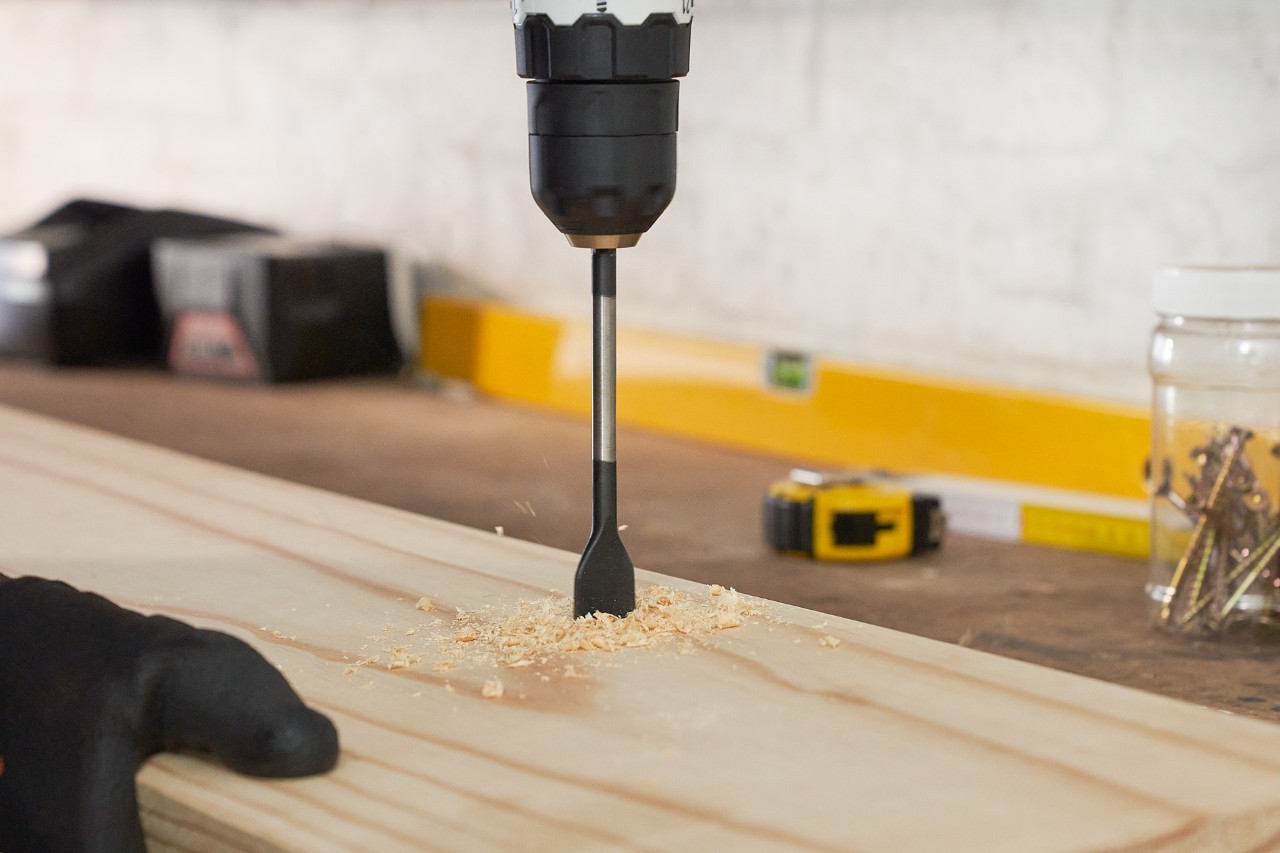  A person drilling holes into a wooden board to build a DIY garden power tool storage rack