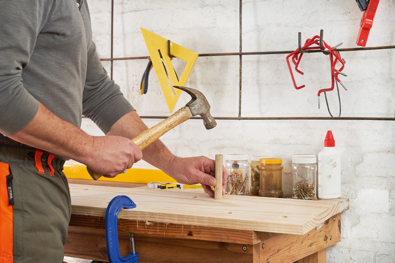 A man using a hammer to tap a dowel into the drilled hole of a wooden board