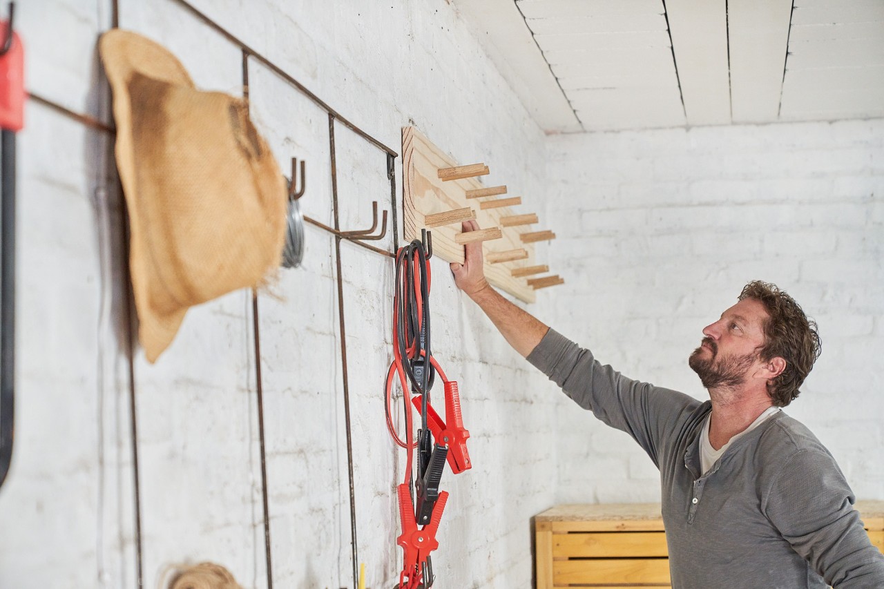 A man standing in front of a DIY power tool storage rack which he has built himself
