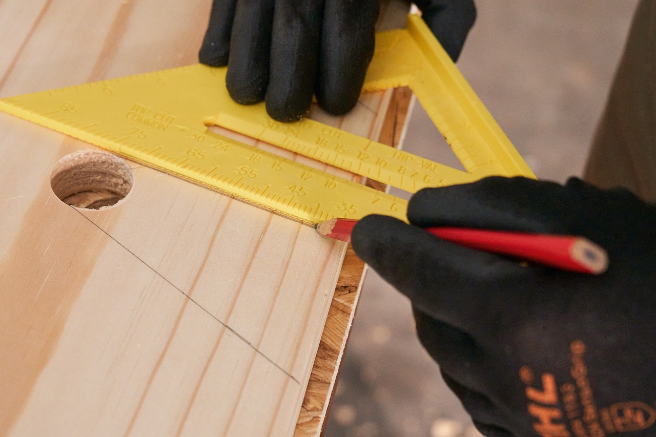 Someone draws lines onto a wooden board using a pencil and set square to mark out the recesses