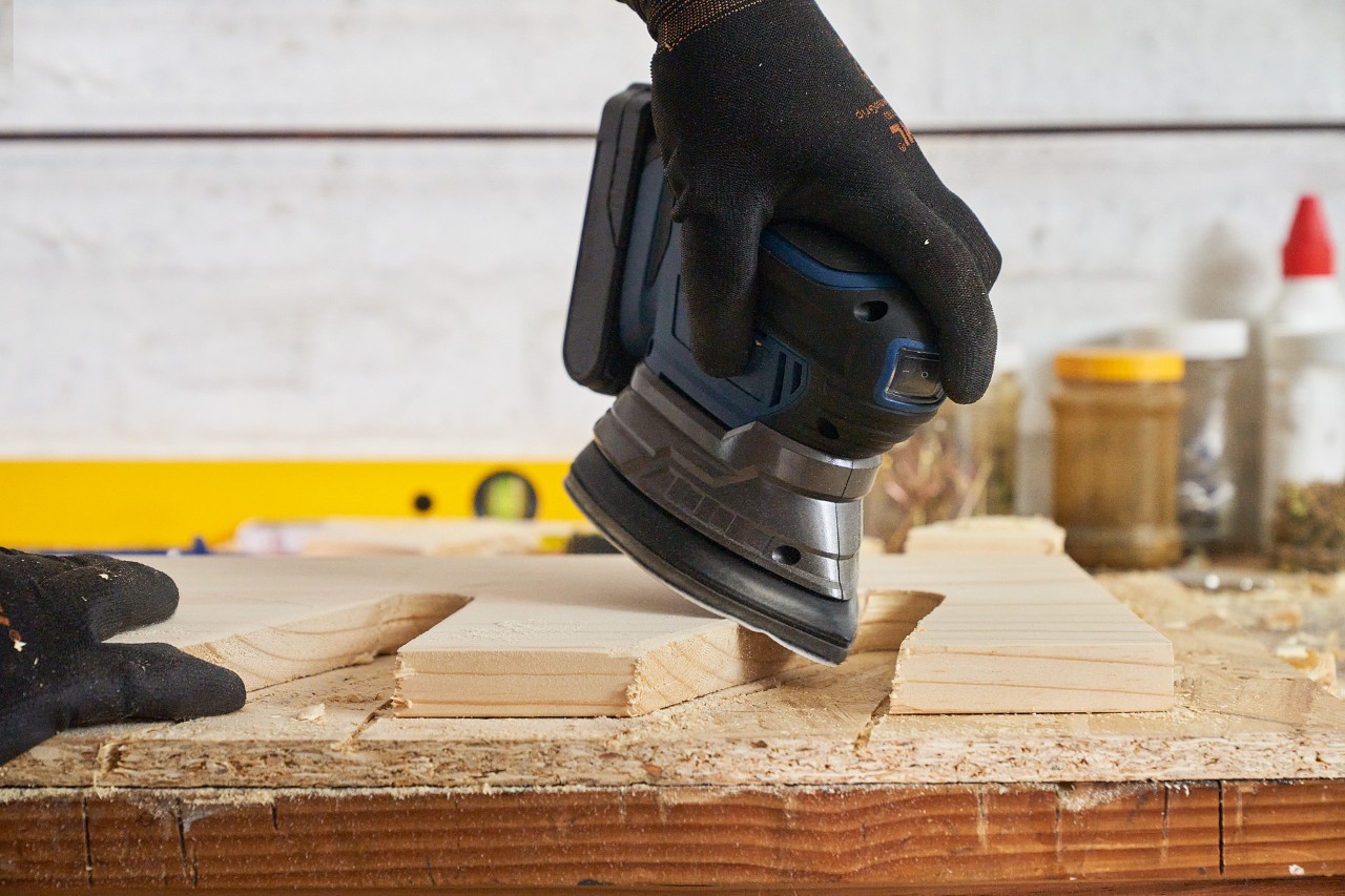 Someone sanding a wooden board with a sander to prevent sharp corners and edges on the garden power tool holder