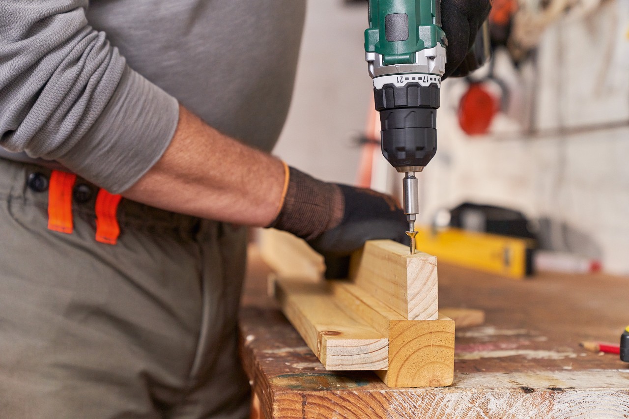 A man screwing battens to uprights to build a DIY lawn mower storage box