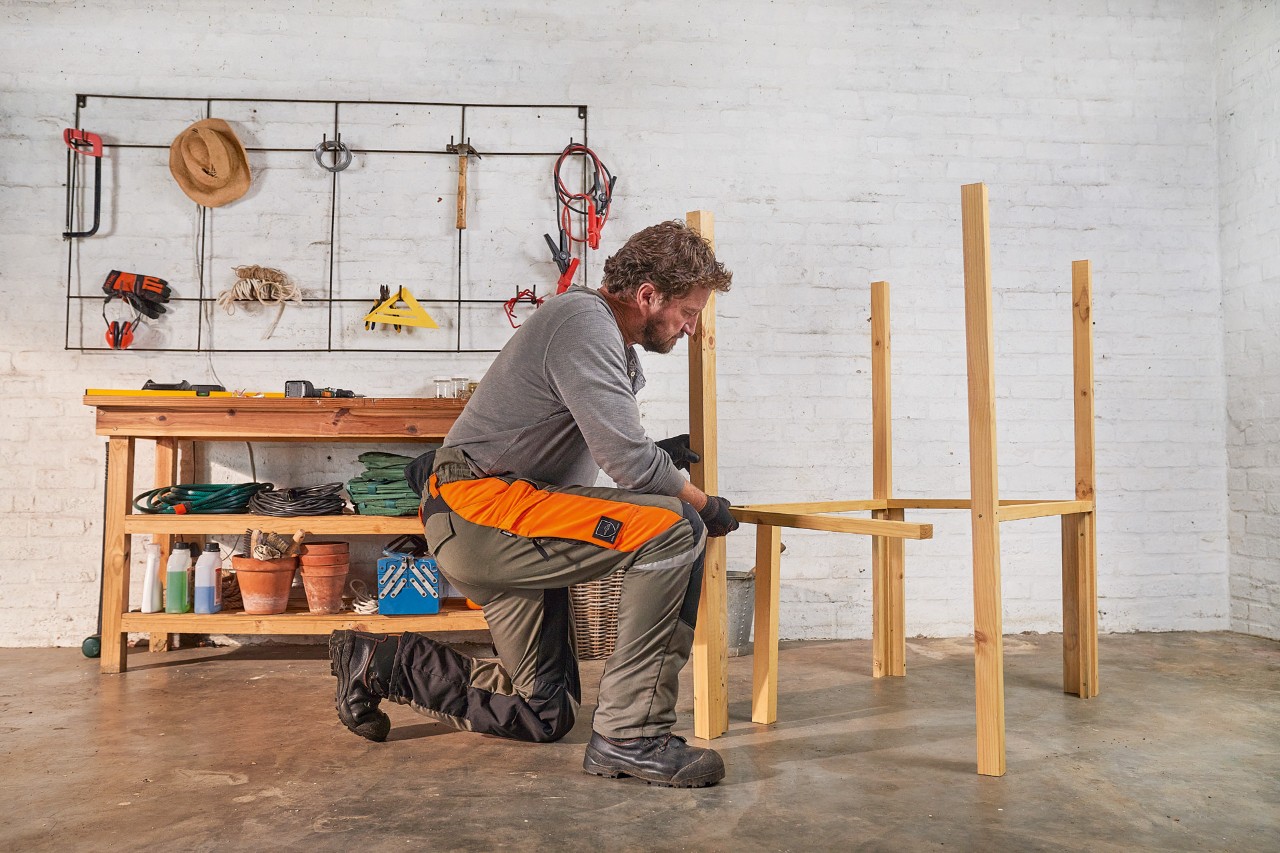 A man screwing cross beams to uprights to build a DIY lawn mower storage box 