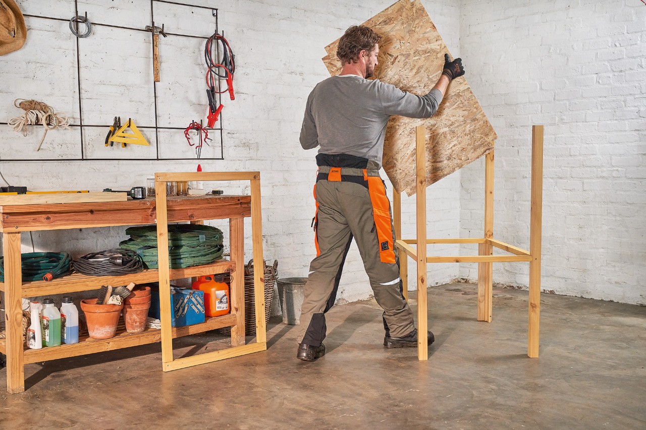 A man installs an OSB board as a raised base for the lawn mower storage box