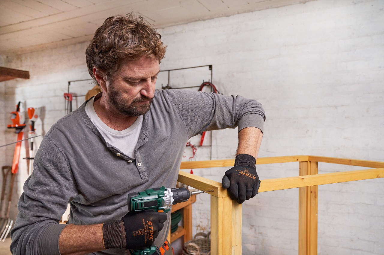 A man using wooden beams to assemble a roof frame for a lawn mower storage box