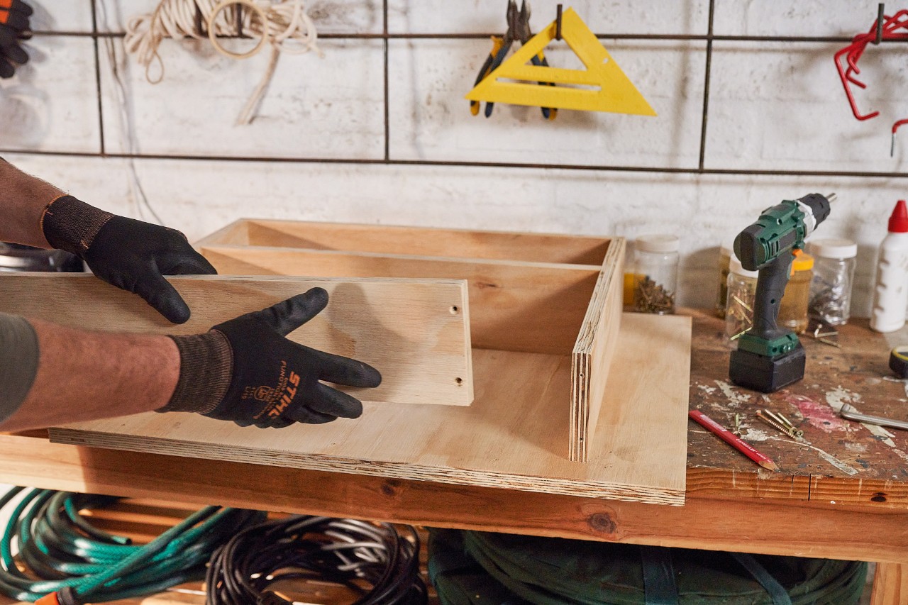 A man building a drawer from wooden boards for the lawn mower storage box 