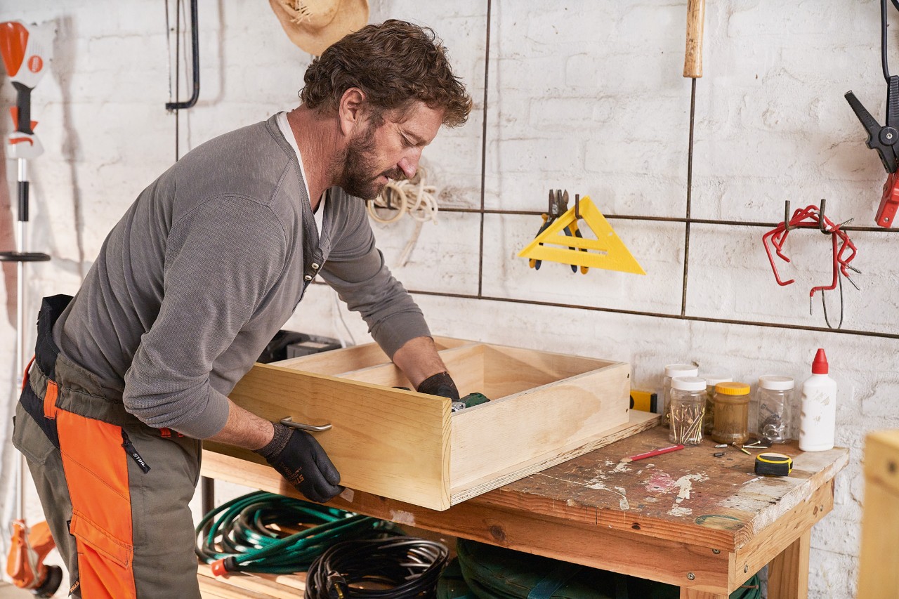 A man mounting a pine board to a drawer to build a DIY lawn mower storage box