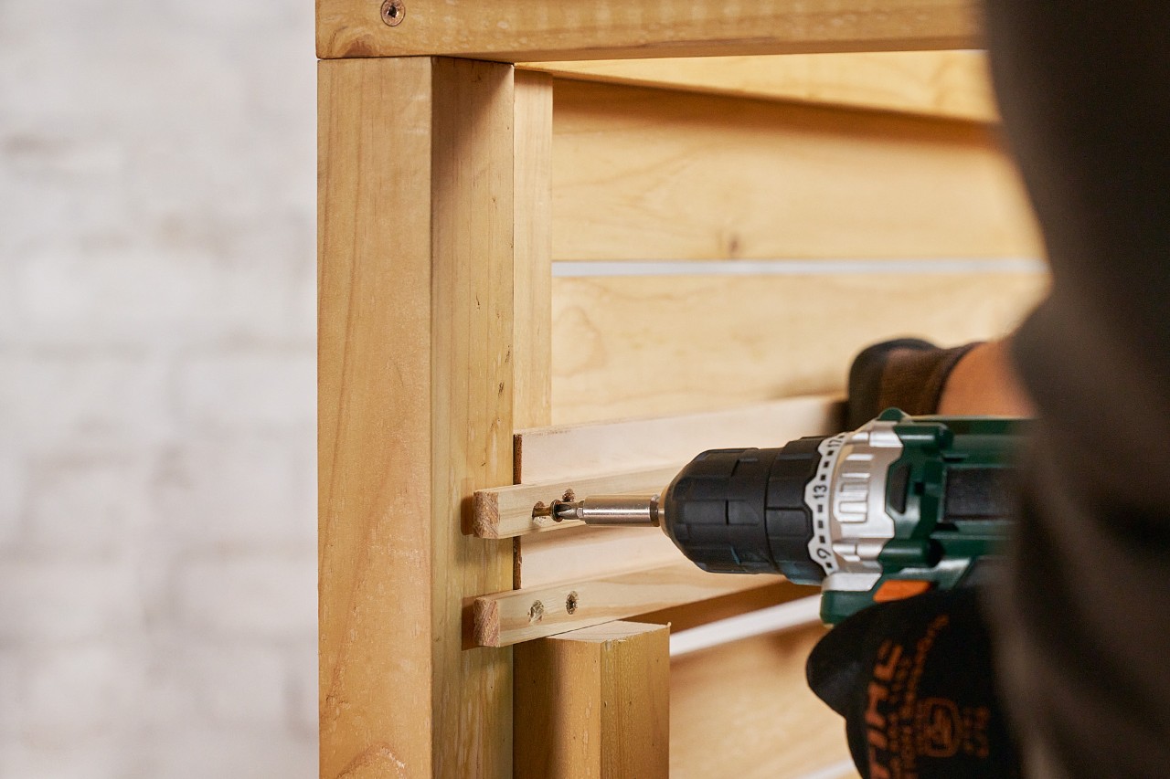 A person using a cordless screwdriver to fit two slide rails to build a DIY lawn mower storage box