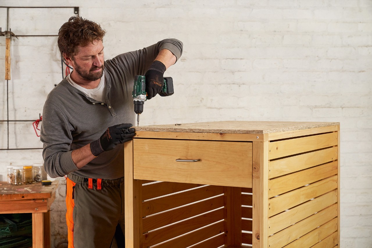 A man mounting an OSB board as a roof onto a lawn mower storage box