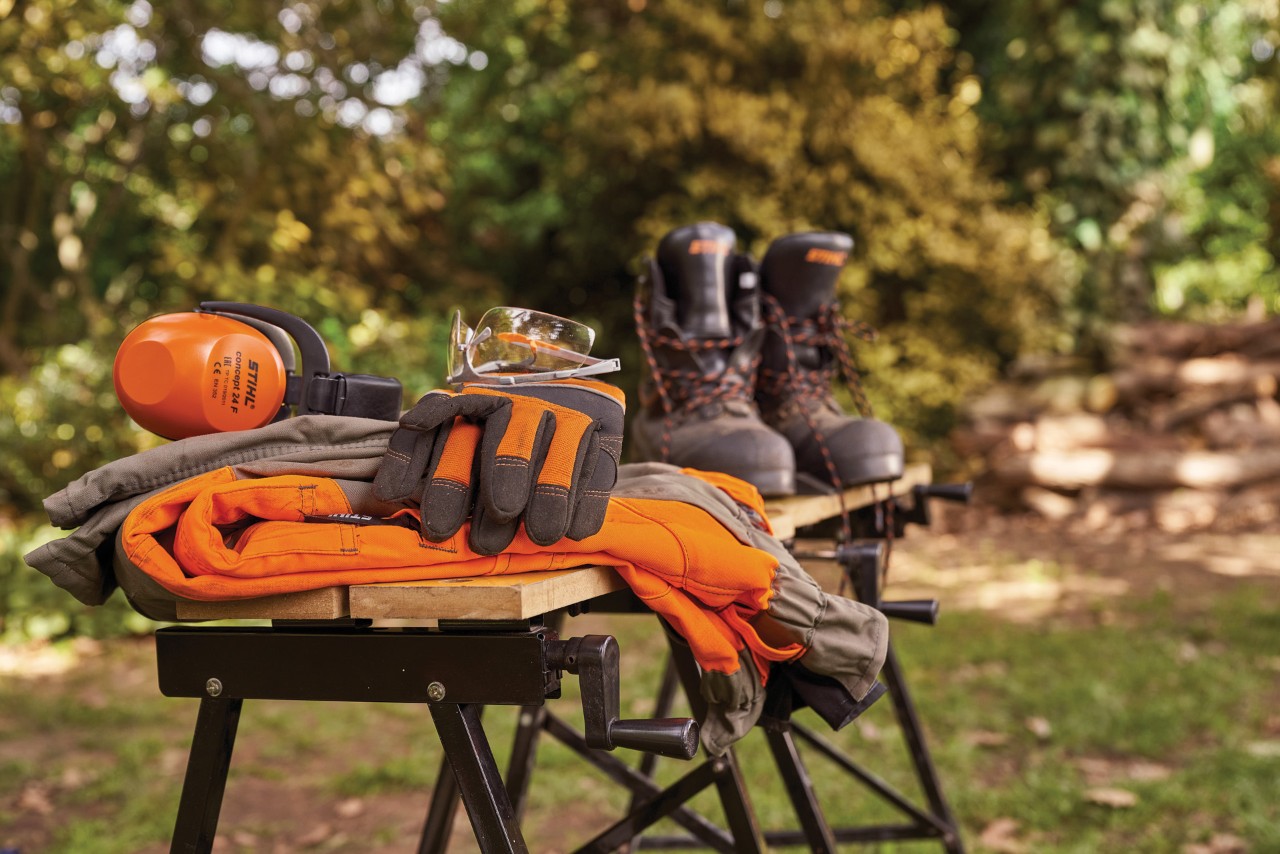 STIHL ear protection, boots, safety glasses, and protective gloves on a workbench in a garden