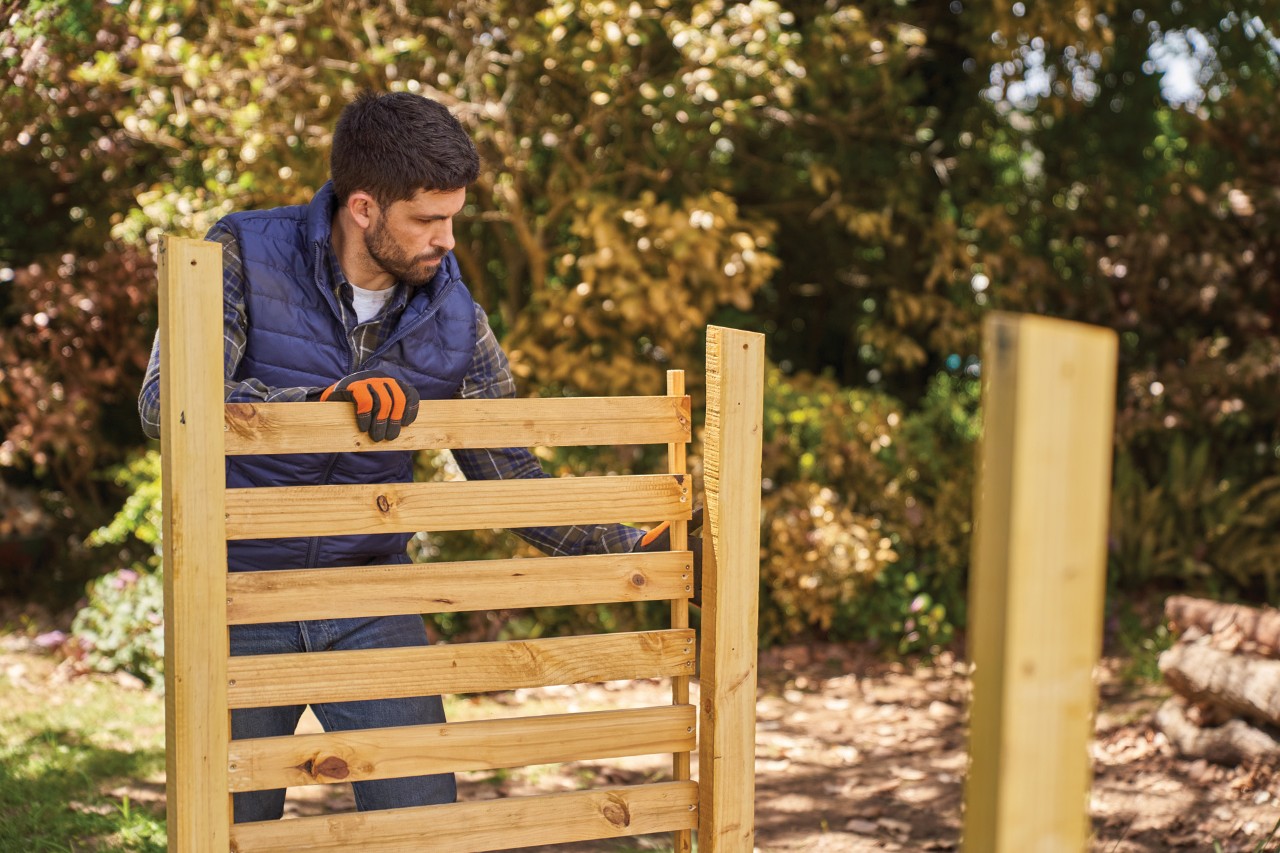 A man attaching the side wall of a DIY log store
