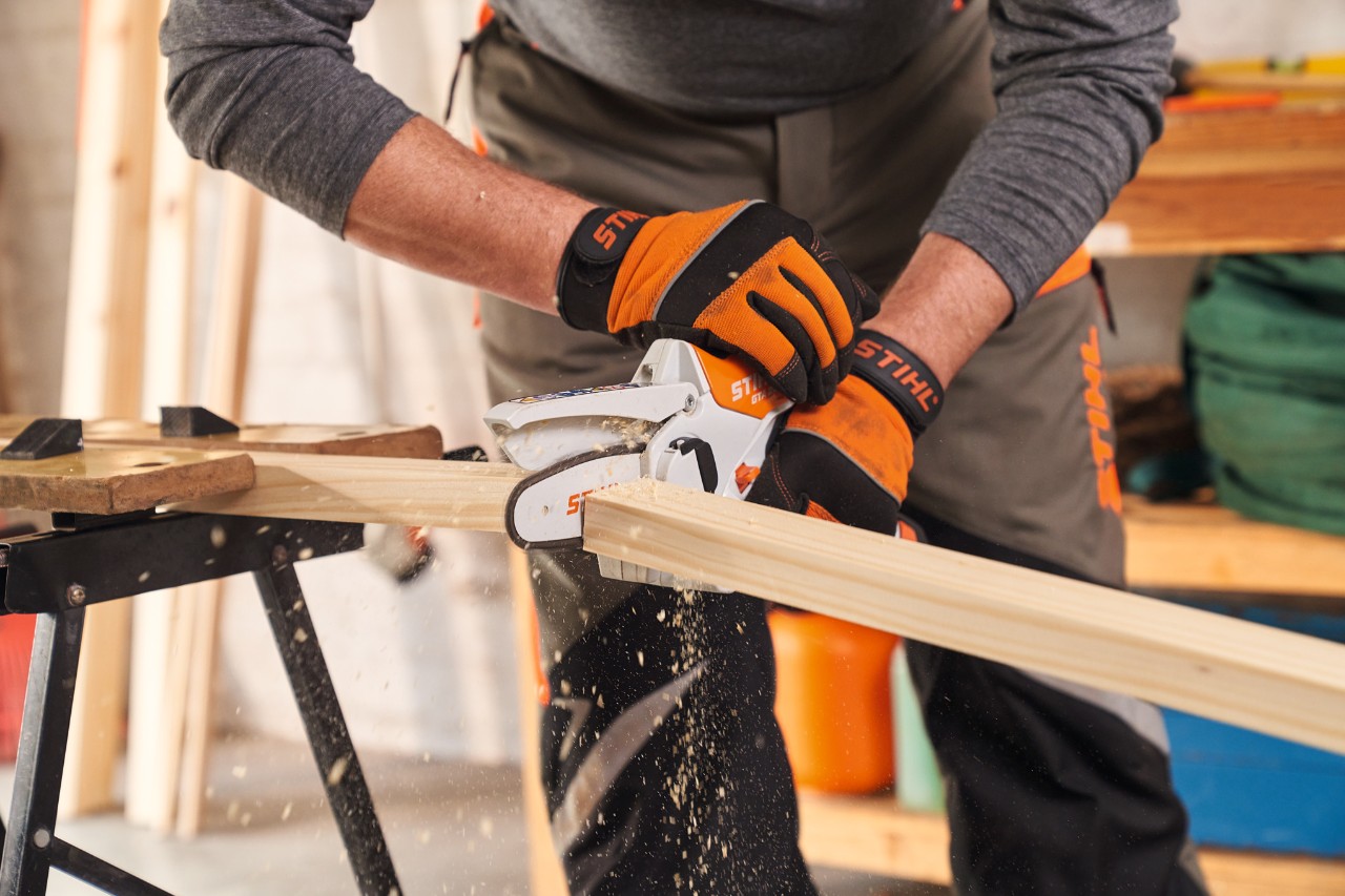 A person wearing STIHL protective gloves cuts frame pieces for a DIY privacy screen to length