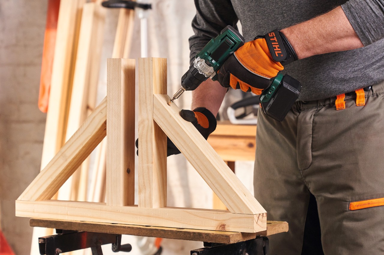 A person wearing STIHL protective gloves screws together the feet for a DIY wooden privacy screen