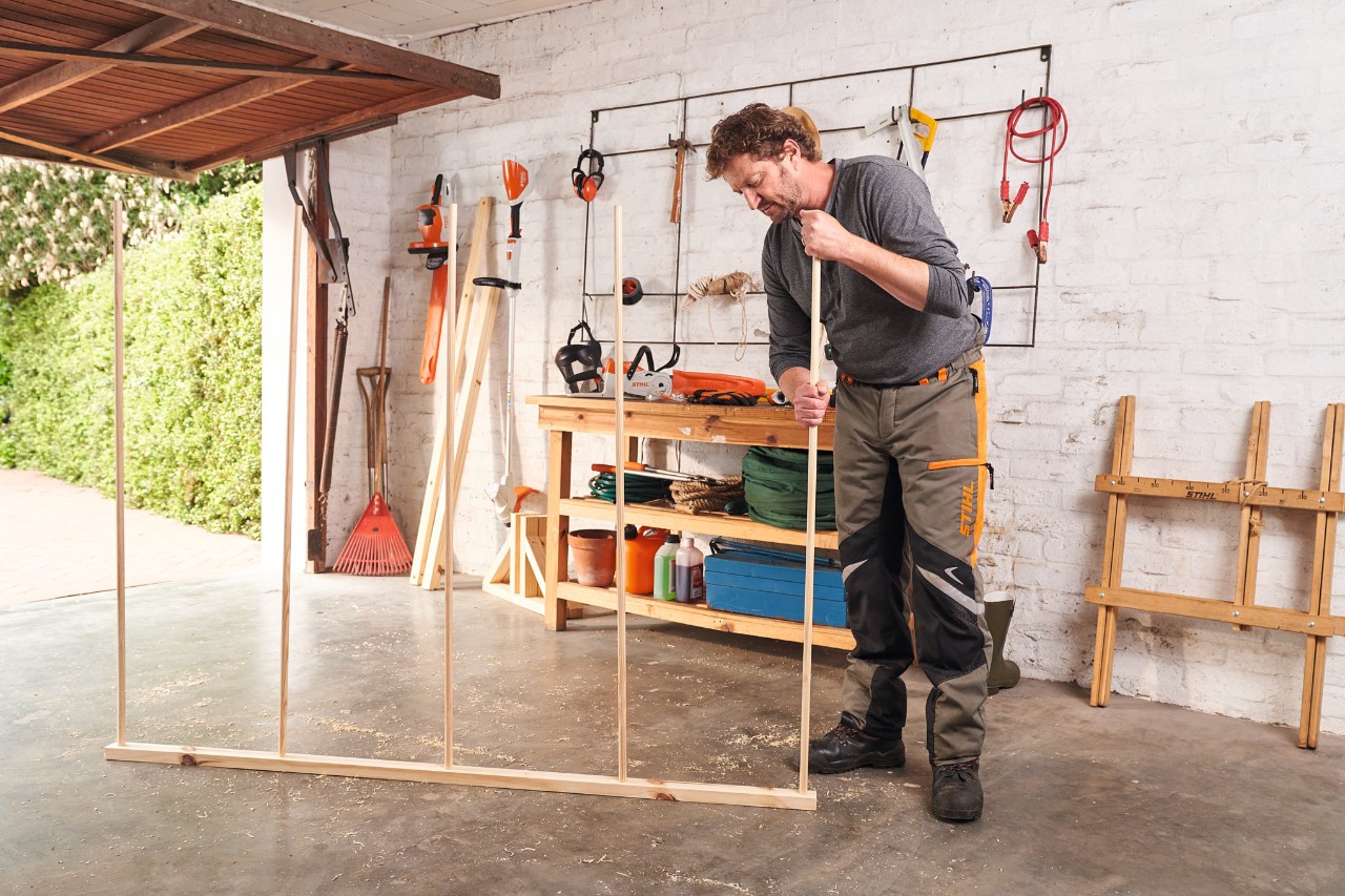 A man in a garage assembling round rods for a DIY wooden privacy screen