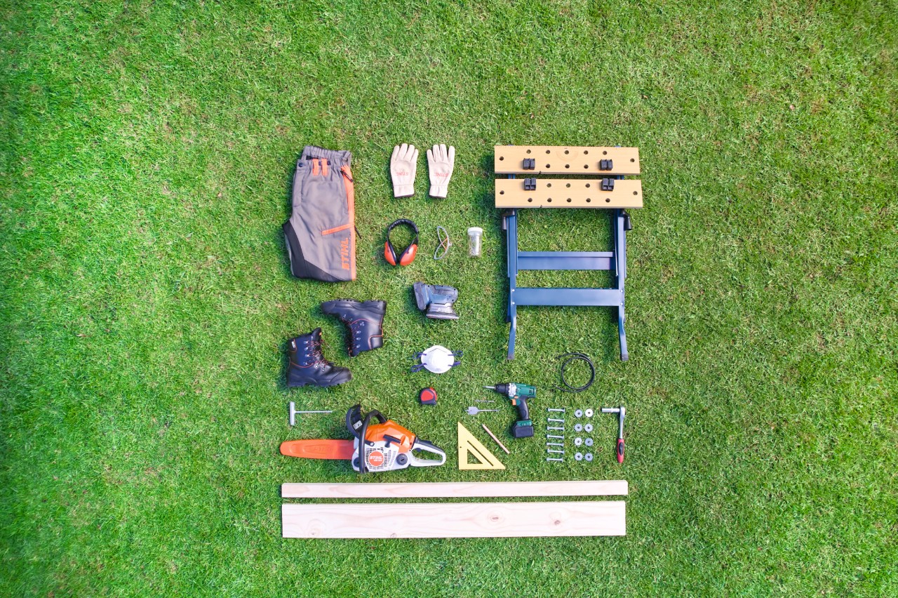 Tools and materials for a DIY sawhorse arranged in a square on grass 