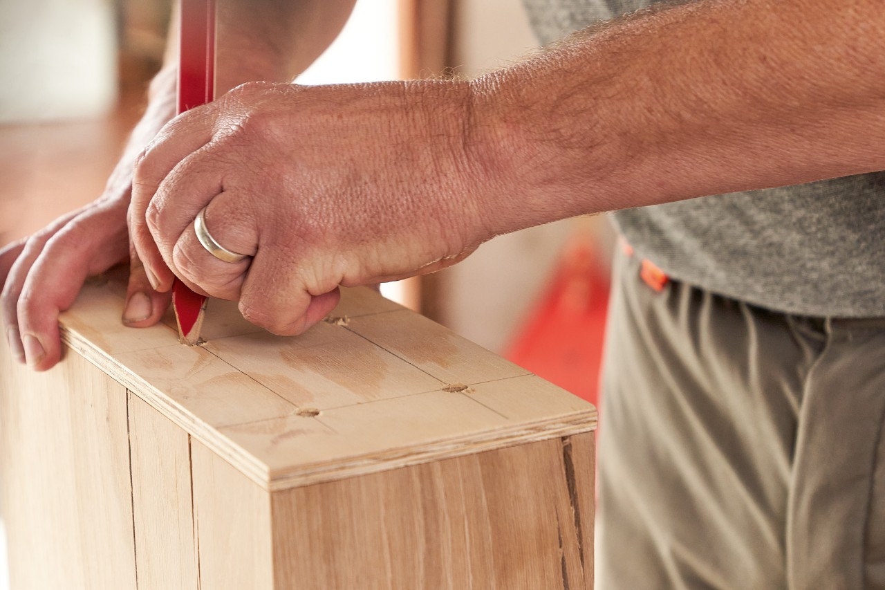A man marking drilling points on a wooden beam with the aid of a template