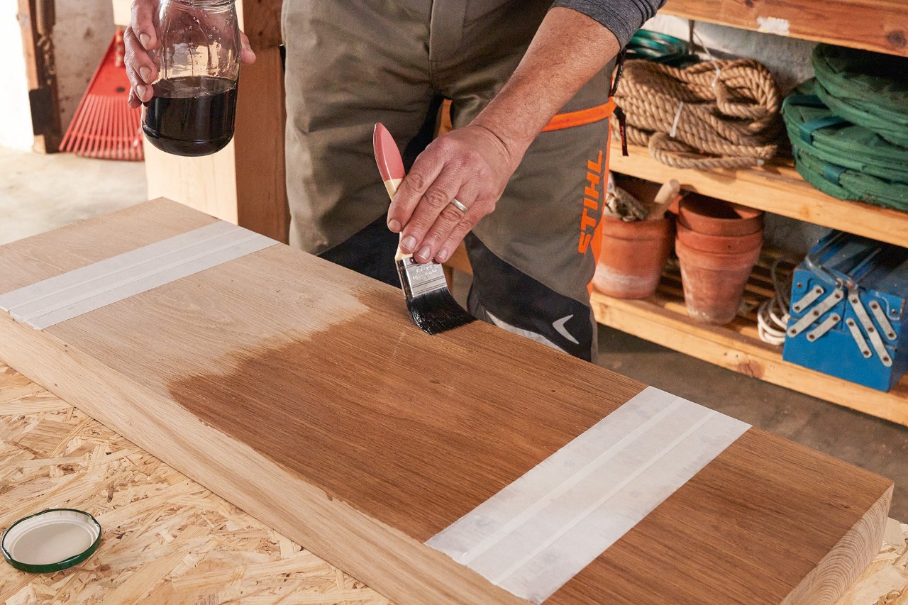 A man wearing STIHL cut-protection trousers oiling a wooden beam using a brush