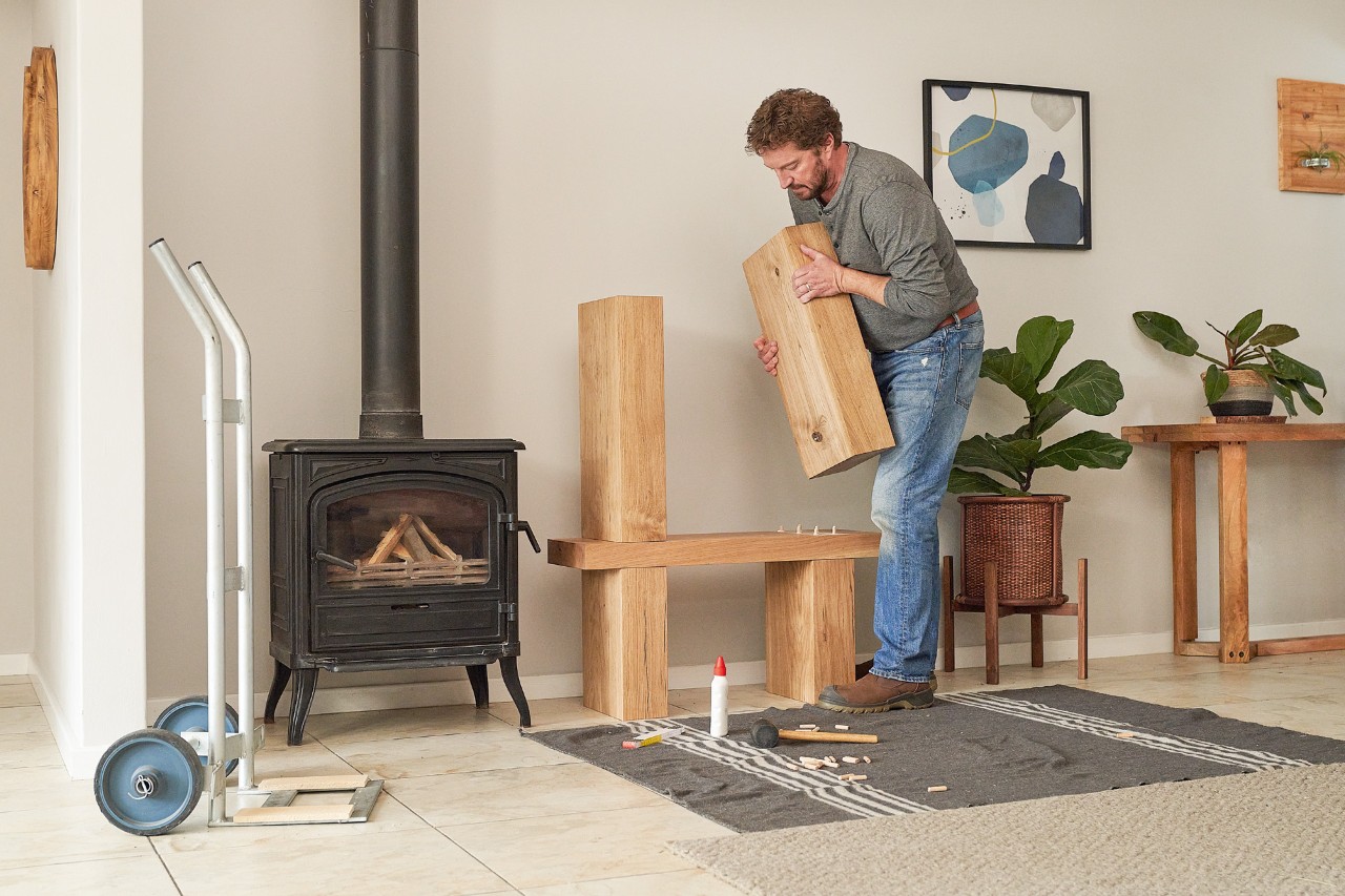 A man working indoors, putting wooden beams together for a firewood rack