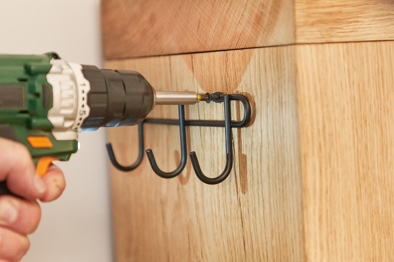 A person with a drill attaching a hook rail to a DIY firewood rack.