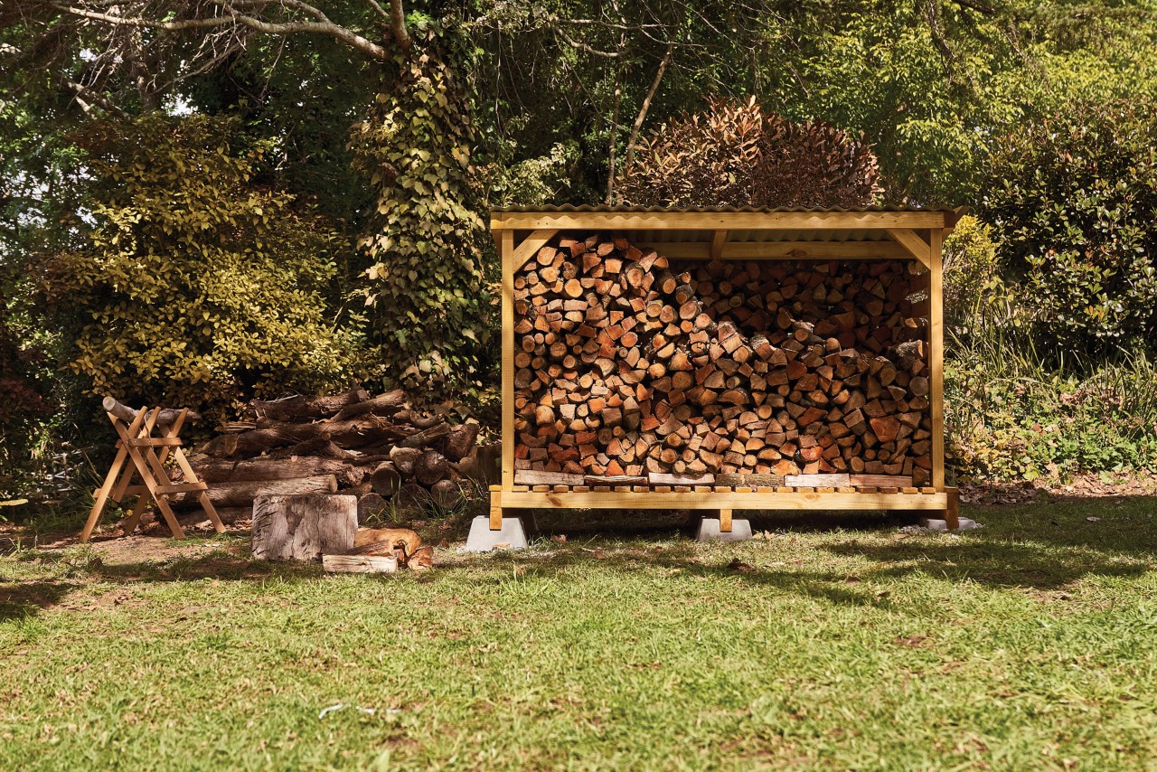 Firewood shelter filled with logs, in a garden