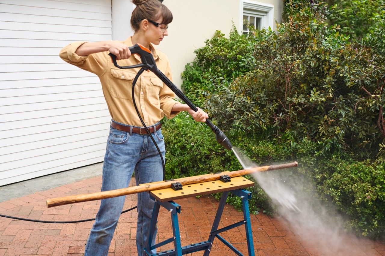 A woman in her driveway uses a STIHL RE 110 high-pressure cleaner to debark a branch on a workbench