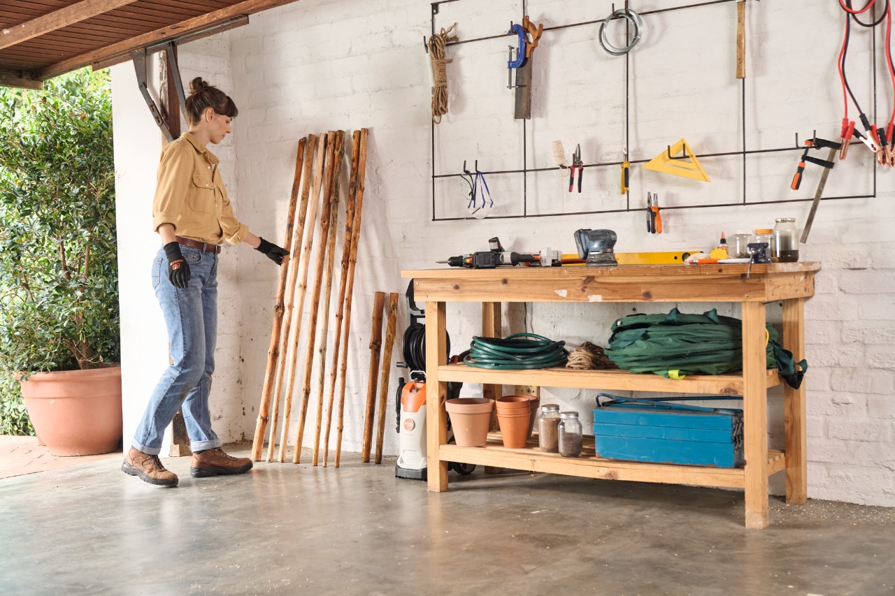 A woman puts debarked wood for a DIY clothes rack in a garage to dry out