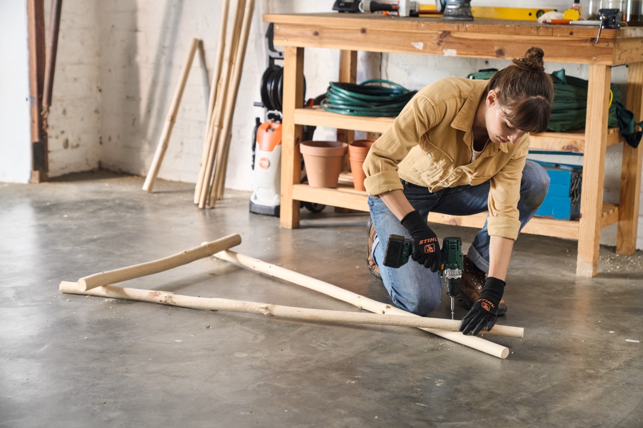 A woman uses a cordless screwdriver to screw together timbers for a DIY clothes rack 