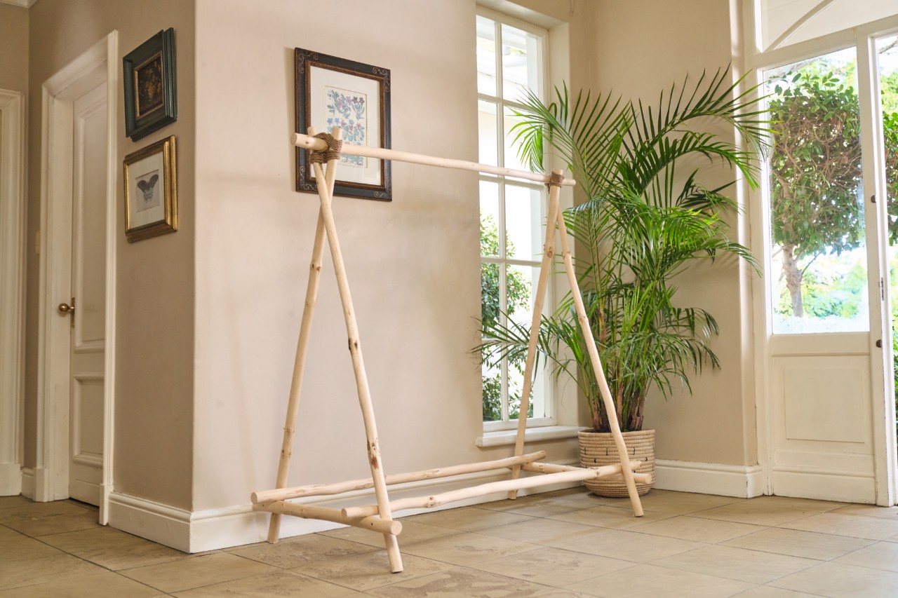 A DIY wooden clothes rack in a room with a potted plant and picture frame in the background