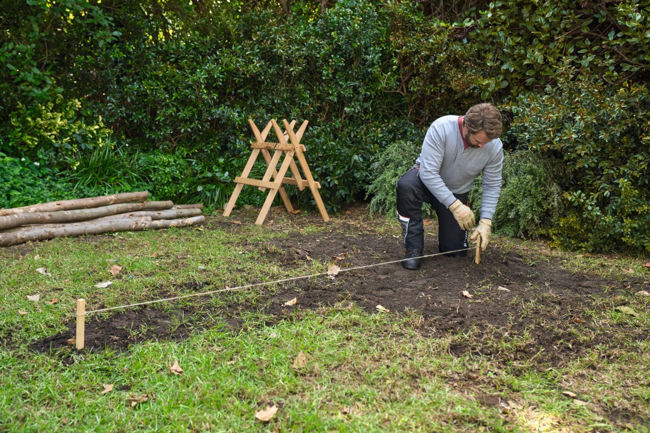 A man inserts small stakes connected by twine into the ground, to mark out the area
