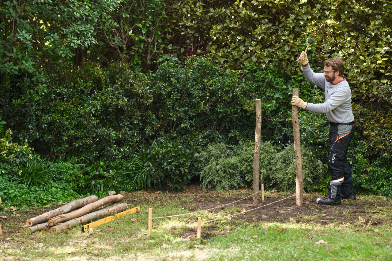 A man hammers in two tree poles as corner points for the dead hedge