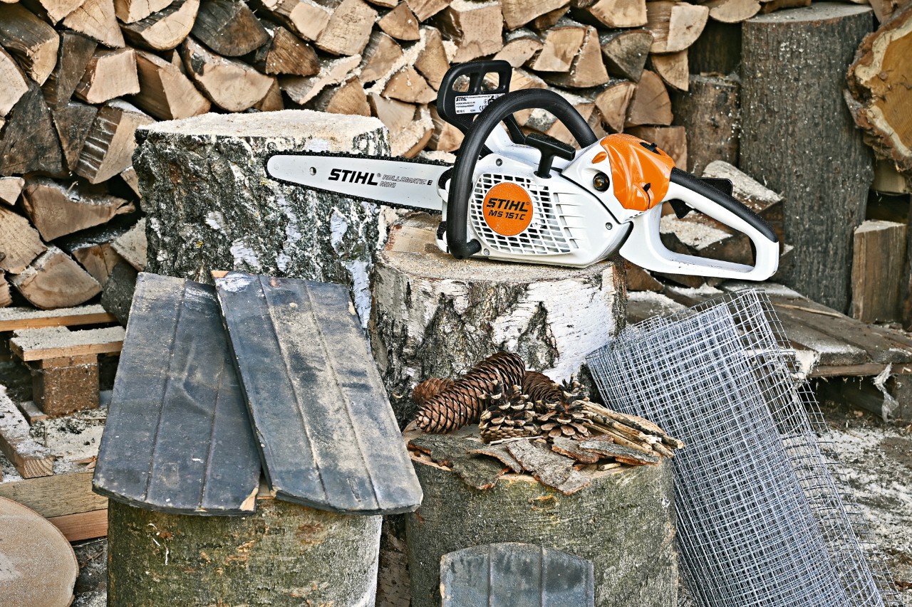 A  STIHL MS 151 C electric chainsaw, wire mesh, roof tiles, pine cones and bark sit on top of three tree stumps