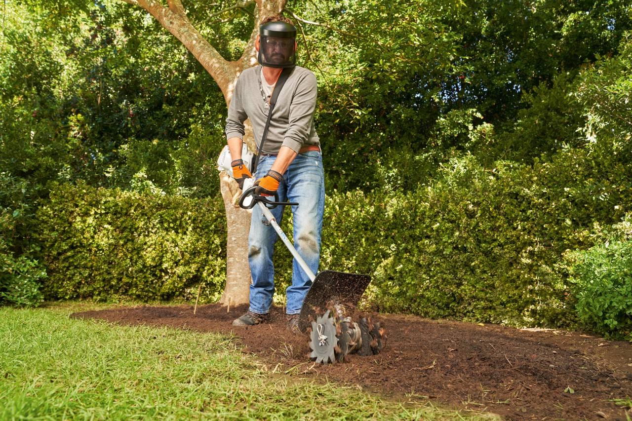 A man working humus into the soil with a STIHL KM 56 RC-E CombiSystem