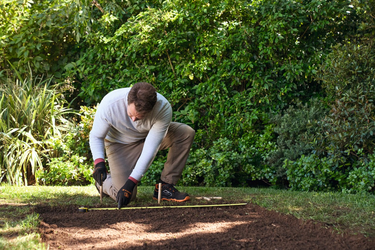 A man marking the sides of the path with stakes and planting string